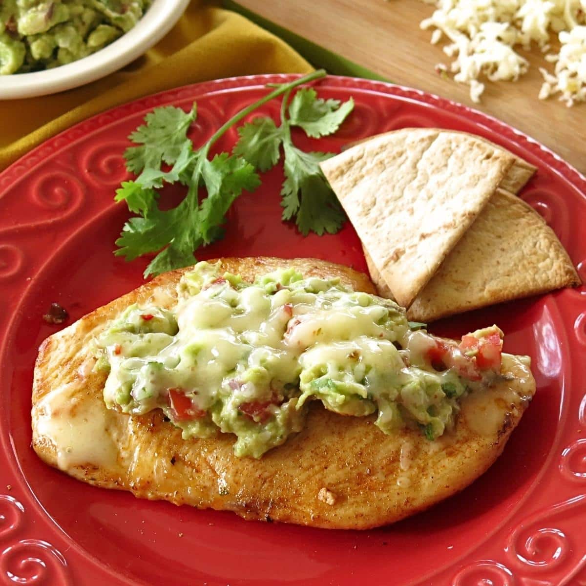 Guacamole Chicken on a red plate with cilantro and homemade low-carb tortilla chips.