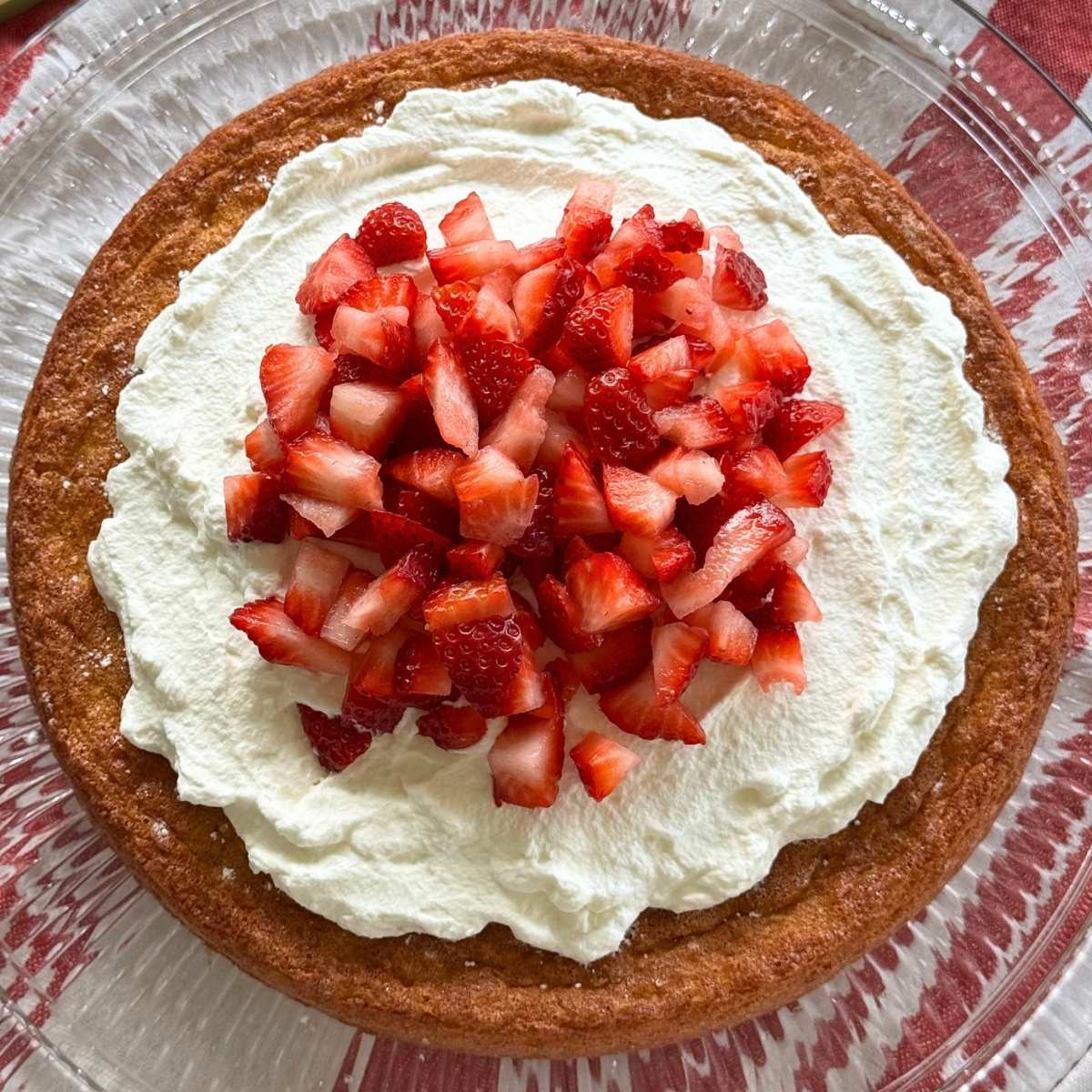 Flourless lemon almond cake topped with whipped cream and chopped strawberries.