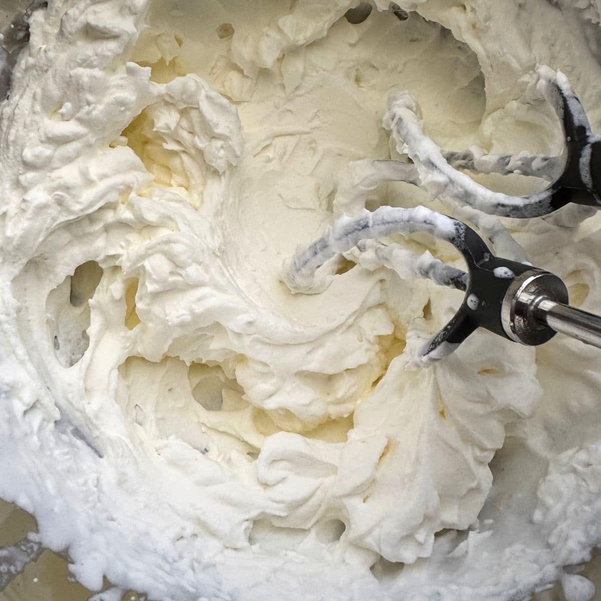 Heavy cream and sweetener whipped in a bowl with beaters inserted.