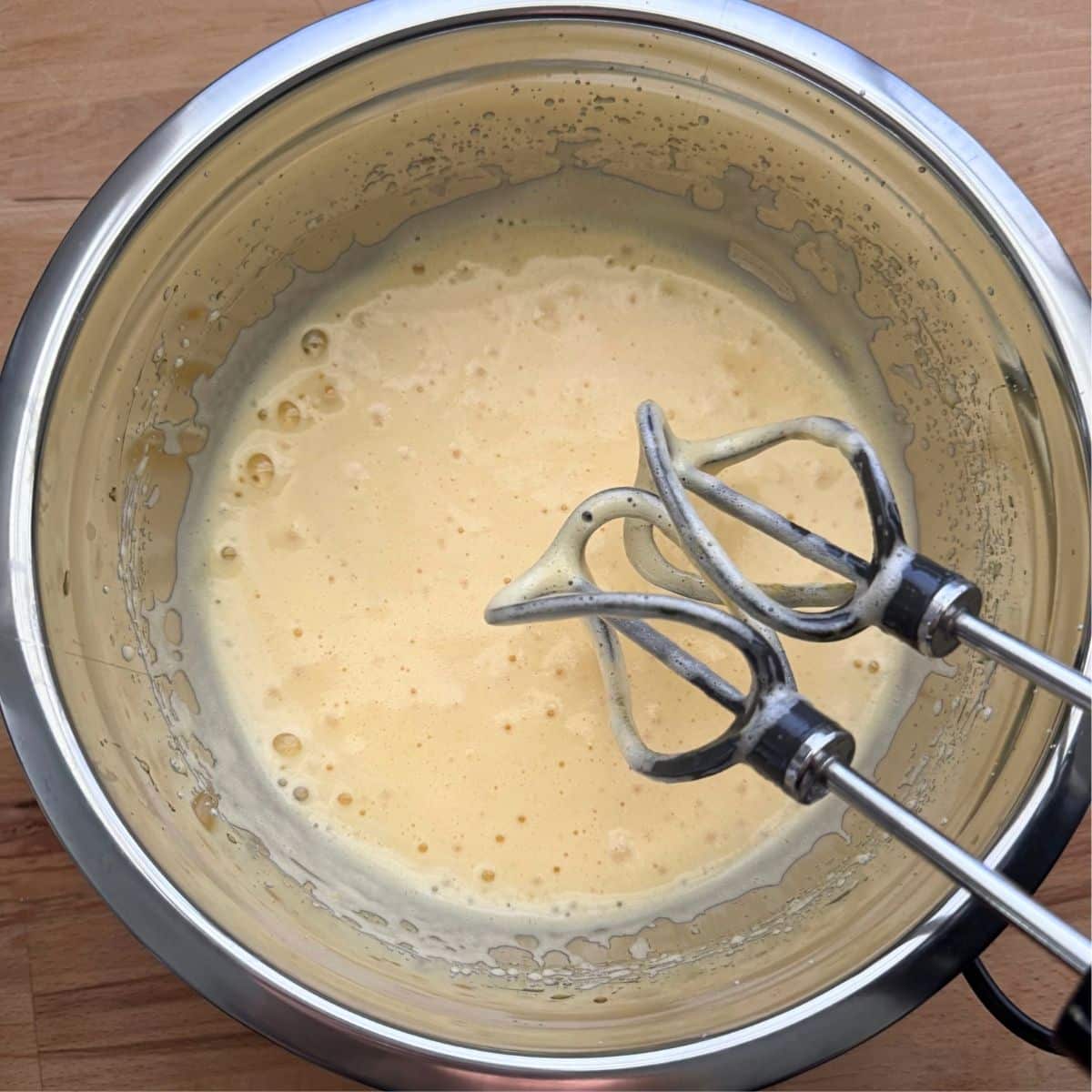 Beaters over whipped eggs and sweetener in a stainless steel bowl with two beaters over it.