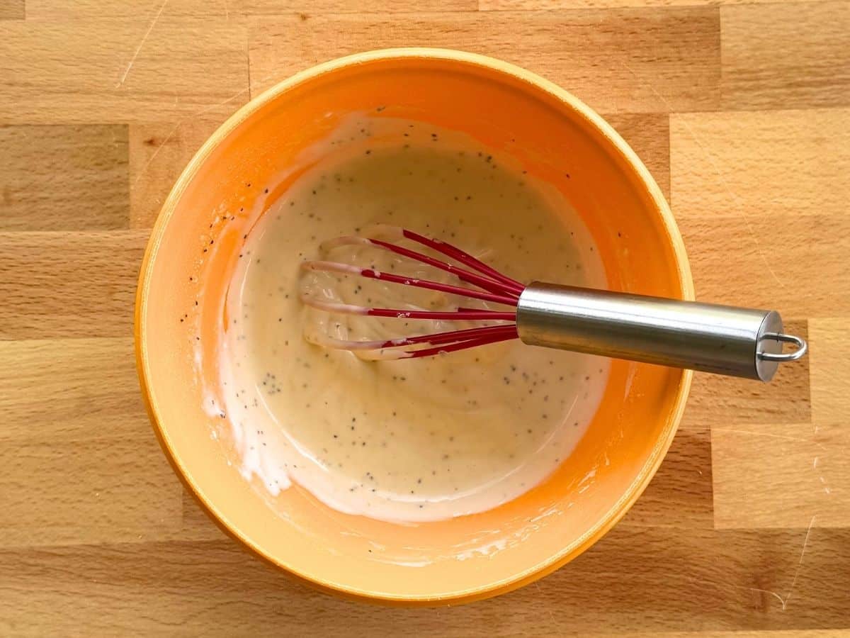 Mixed dressing for cauliflower potato salad in an orange bowl with a whisk.