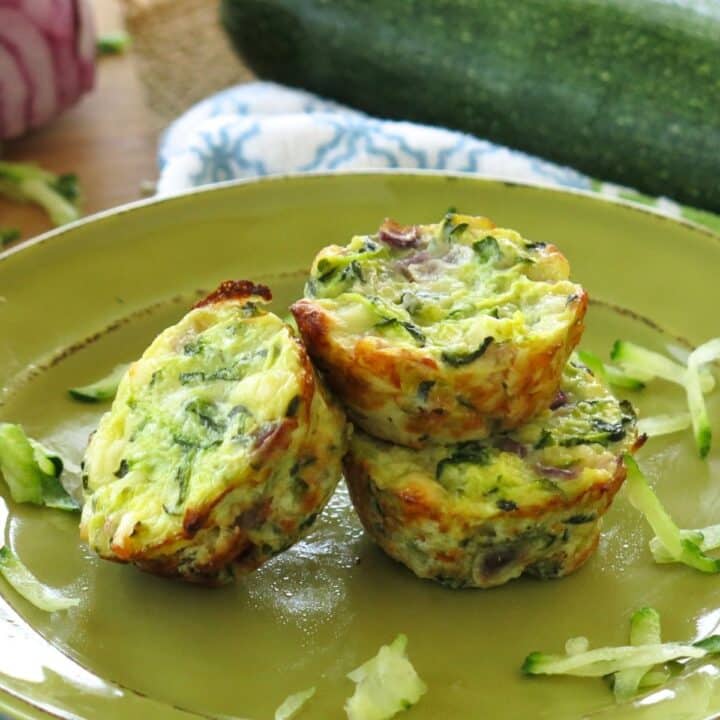 Three zucchini egg muffins on a green plate with a few zucchini shreds on it.