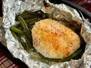 Ranch chicken with ranch dressing and Parmesan cheese on top of green beans in an open aluminum foil packet.