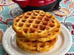 Three cauliflower waffles stacked on top of each other in front of a dash waffle maker.