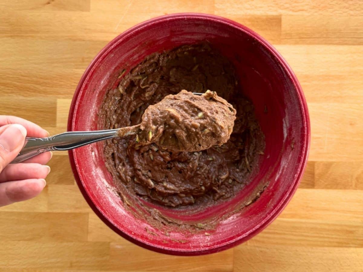 Spoon holding batter to show thickness after shredded zucchini and chocolate chips are incorporated.