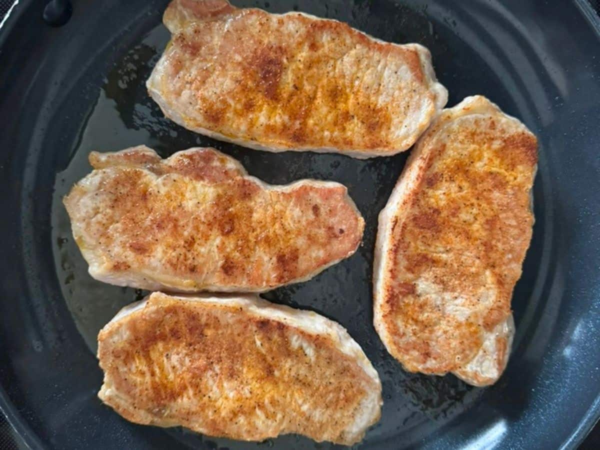 Four seasoned pork chops in a black skillet.