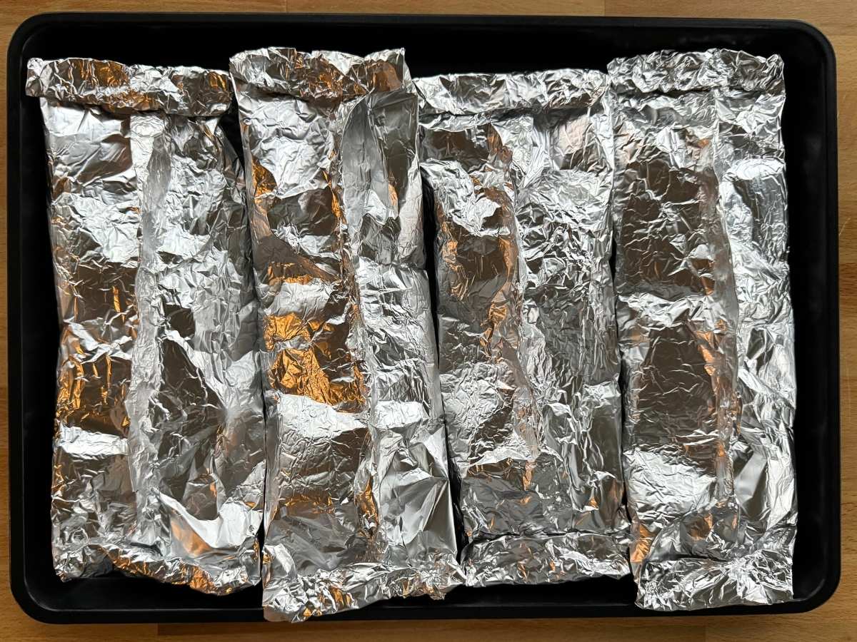 Four foil packets on a baking sheet.