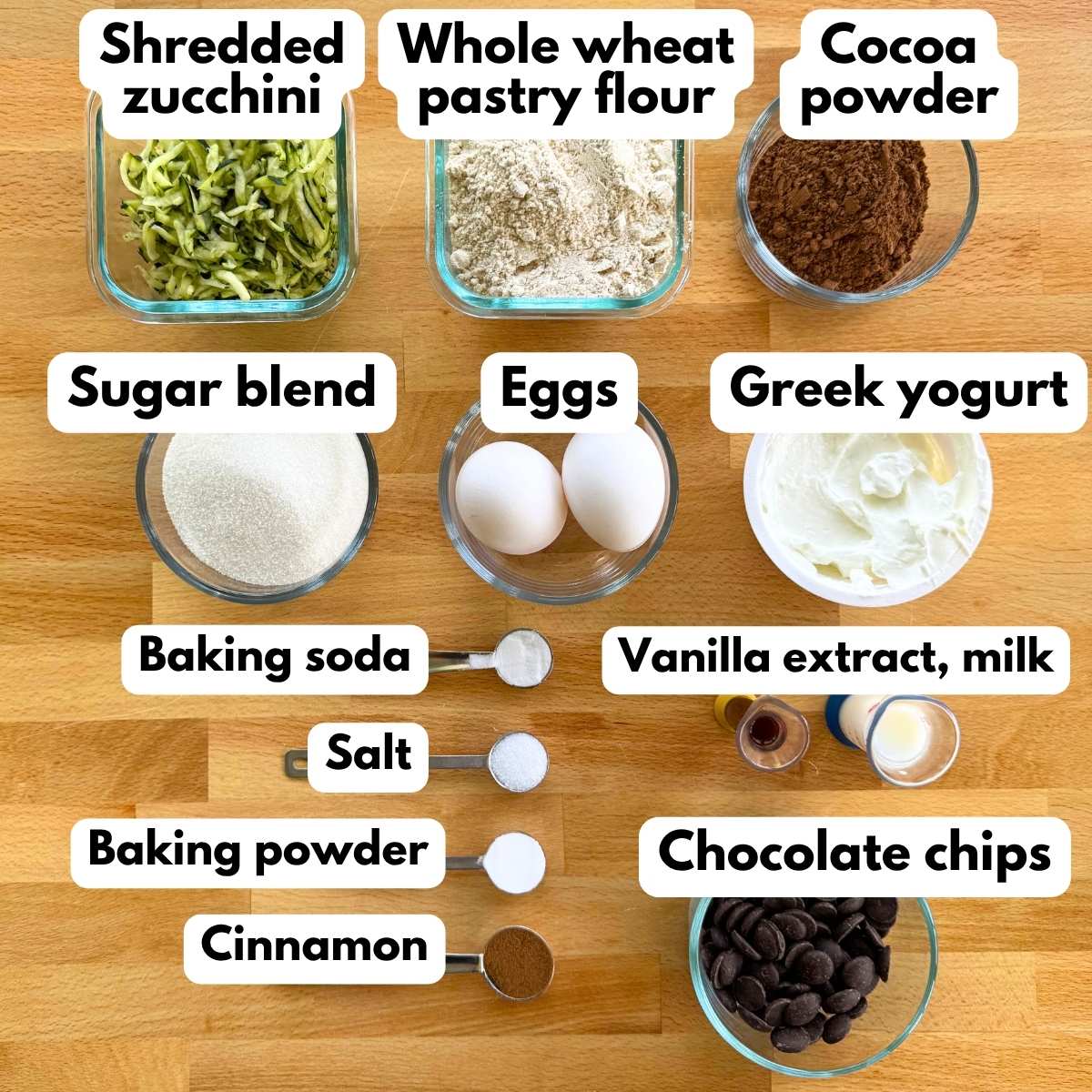 Ingredients for healthy chocolate zucchini muffins: shredded zucchini, Greek yogurt, cocoa powder, whole wheat pastry flour, sugar blend, eggs, baking soda, salt, cinnamon, baking powder, vanilla extract, milk, and chocolate chips.