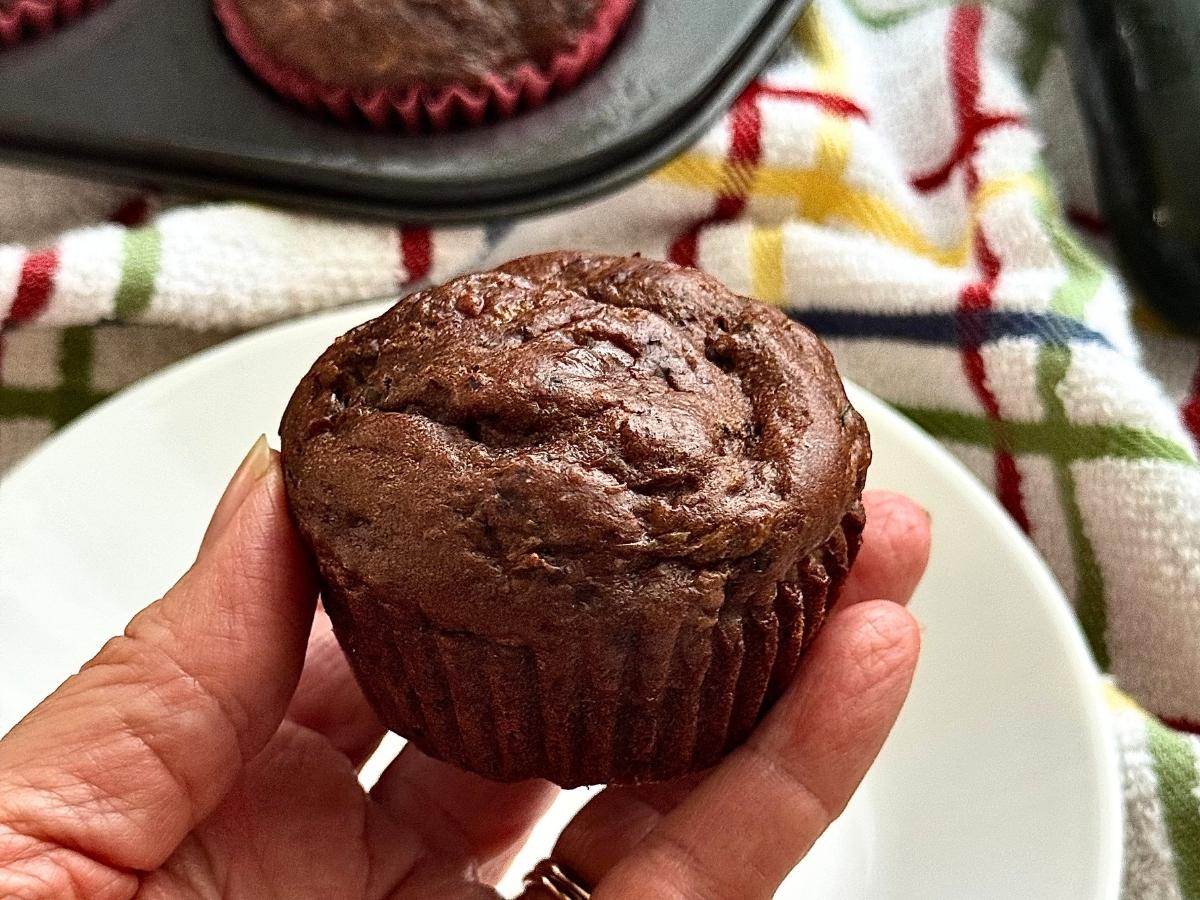 Hand holding a freshly baked healthy chocolate zucchini muffin made with Greek yogurt and chocolate chips.
