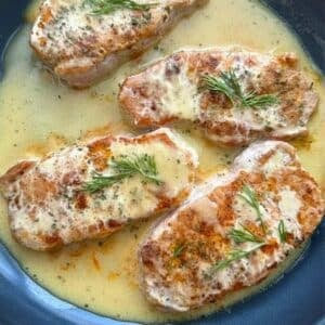 Four pork chops with creamy honey mustard sauce in a large pan.