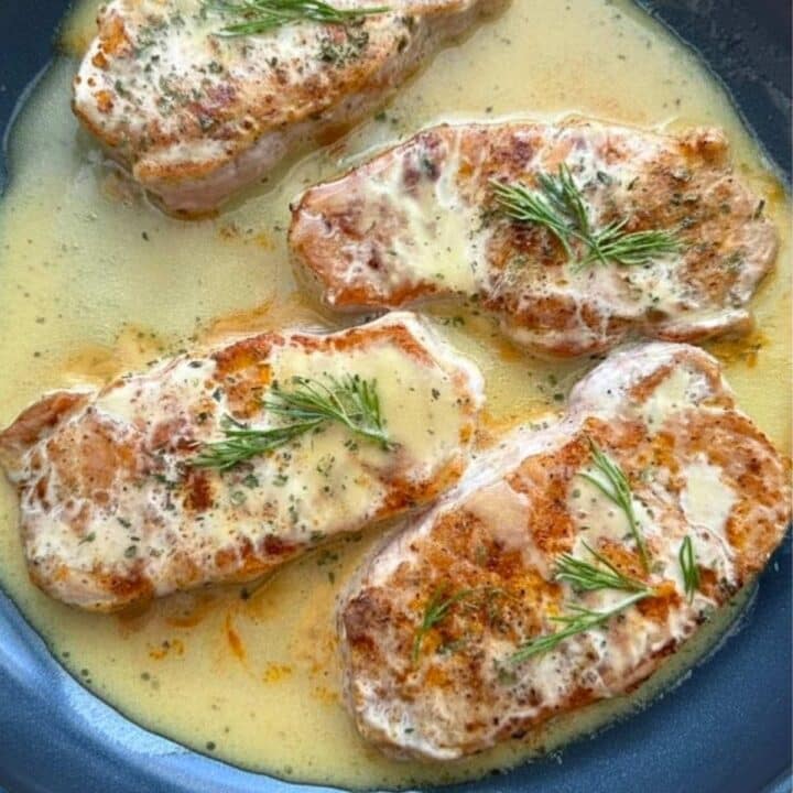 Four pork chops with creamy honey mustard sauce in a large pan.