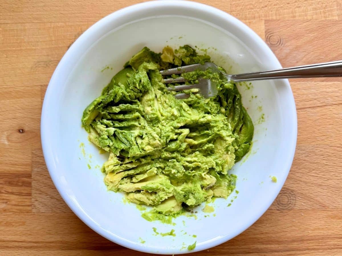 Mashed avocado, lemon juice, and salt mixed togther in a white bowl.