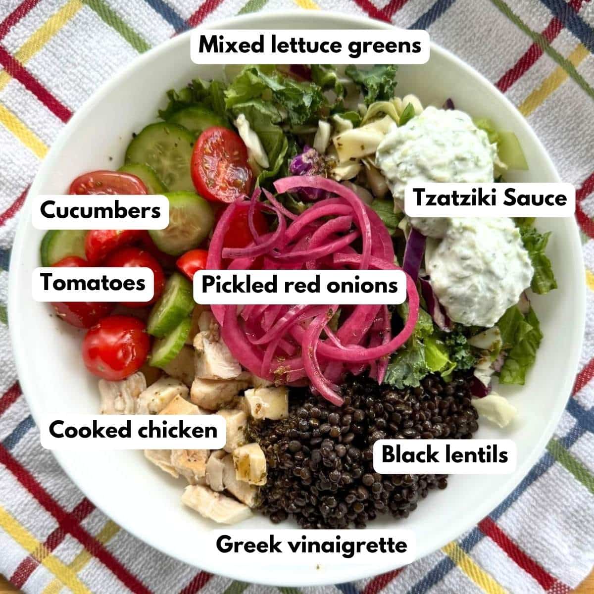 Labeled ingredients for Mediterranean bowls: Mediterranean bowl with black lentils, chicken, salad greens, tzatziki sauce, tomatoes, cucumbers, Greek vinaigrette and pickled red onions.