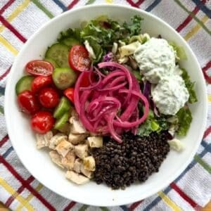Mediterranean bowl with black lentils, chicken, salad greens, tzatziki sauce, tomatoes, cucumbers, Greek vinaigrette and pickled red onions.