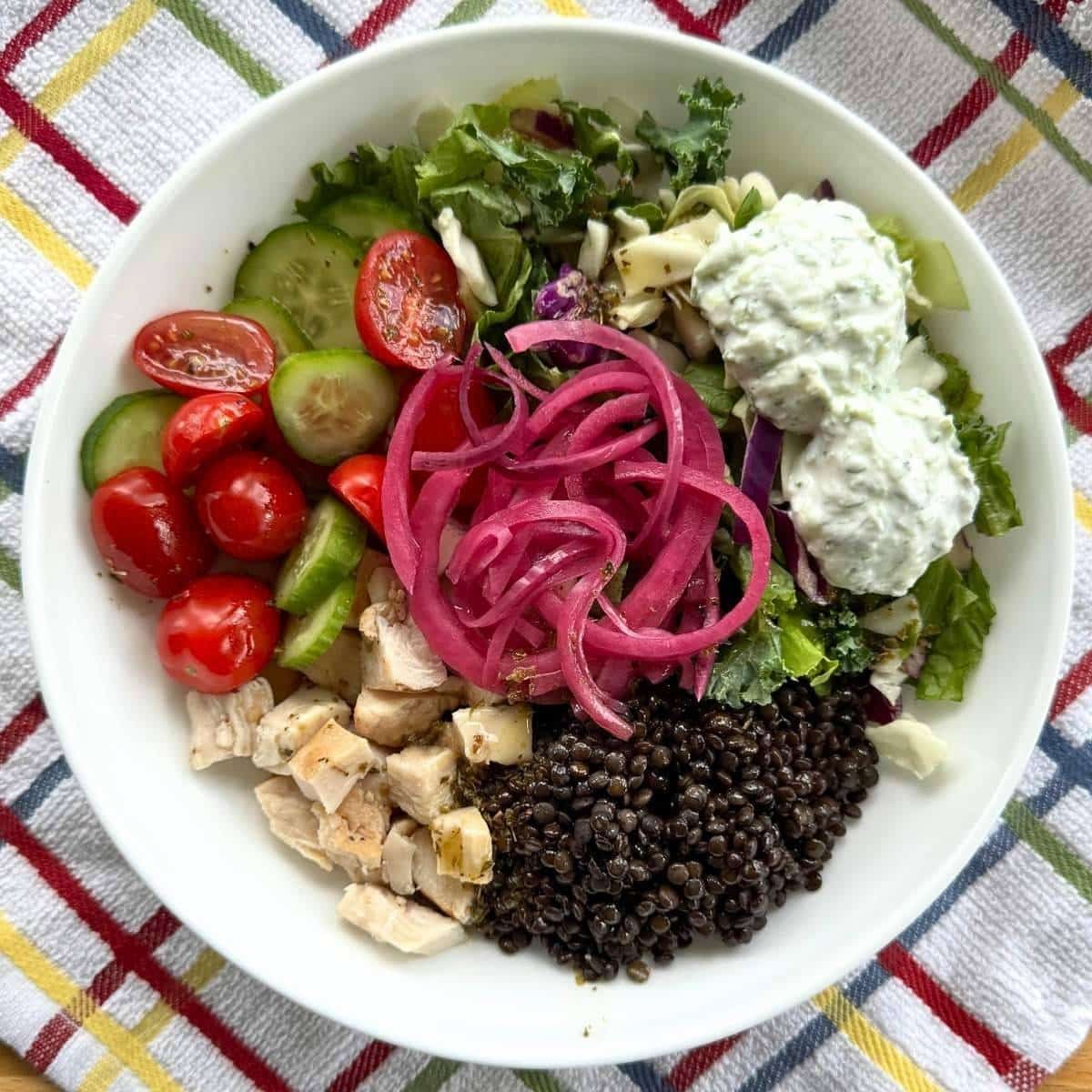 Mediterranean bowl with black lentils, chicken, salad greens, tzatziki sauce, tomatoes, cucumbers, Greek vinaigrette and pickled red onions.