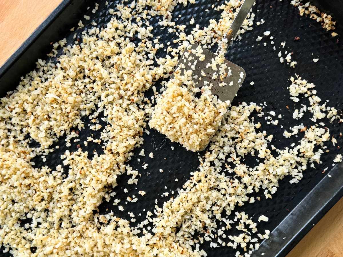 Spatula lifting golden roasted rice cauliflower and brown bits from a sheet pan.