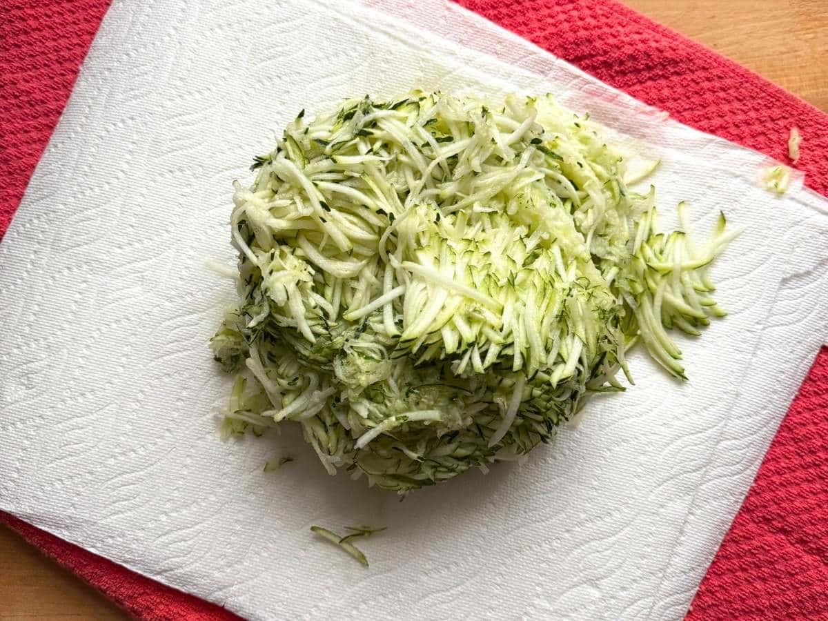 Shredded zucchini on top of paper towels and a dish towel.