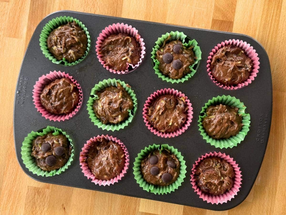 Chocolate zucchini muffin batter portioned into a lined muffin pan before baking.
