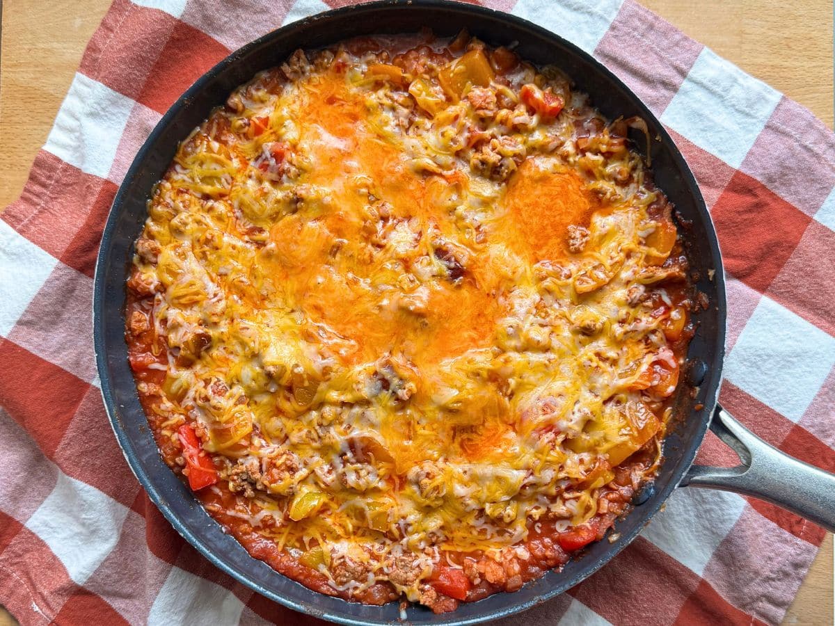 Shredded Monterey Jack cheese melting over unstuffed bell peppers and ground turkey in a skillet.