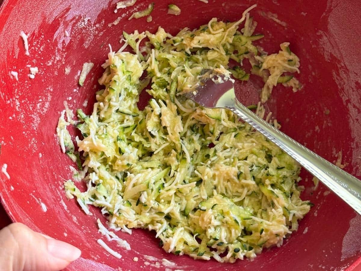 Batter for zucchini chaffles mixed together with a fork in a red bowl.