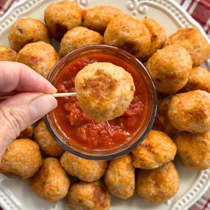 A baked chicken parmesan meatball on a toothpick over a plate with more meatballs and marinara.