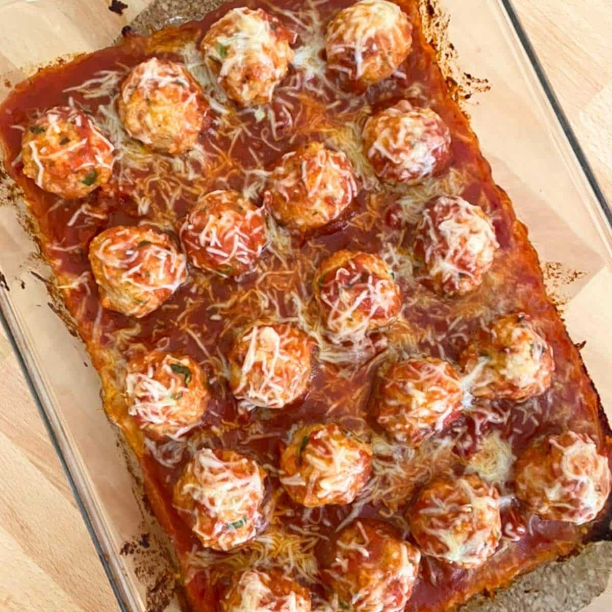 Baked chicken Parmesan meatballs topped with more cheese in a glass baking dish with marinara.