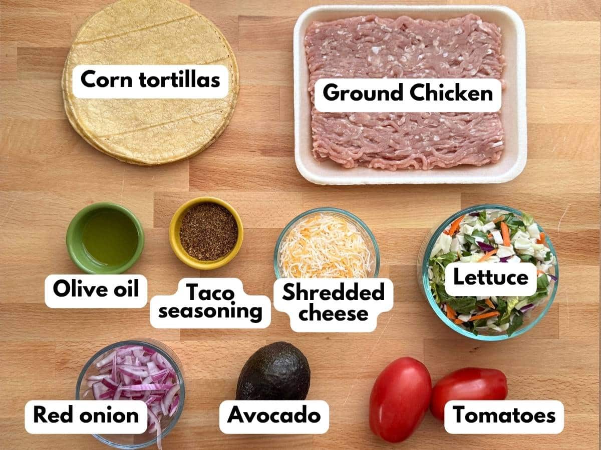Ingredients for ground chicken tacos including corn tortillas, ground chicken, taco seasoning, cheese, lettuce, tomatoes, avocado, and red onion.