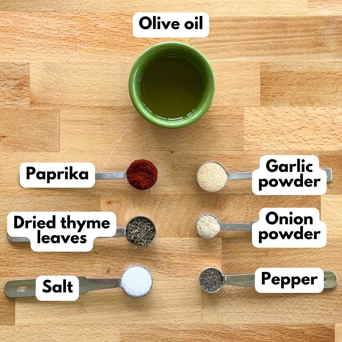 Olive oil, paprika, garlic powder, dried thyme leaves, and onion powder on a cutting board.