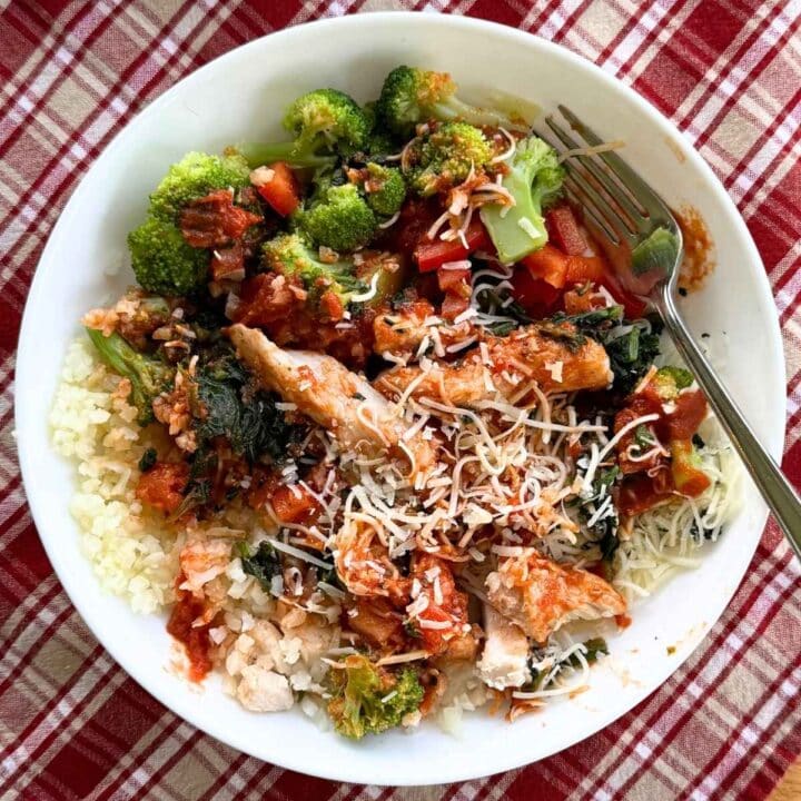 Chicken marinara meal prep bowl with cauliflower rice, vegetables, marinara, chicken and melted cheese in a white bowl.