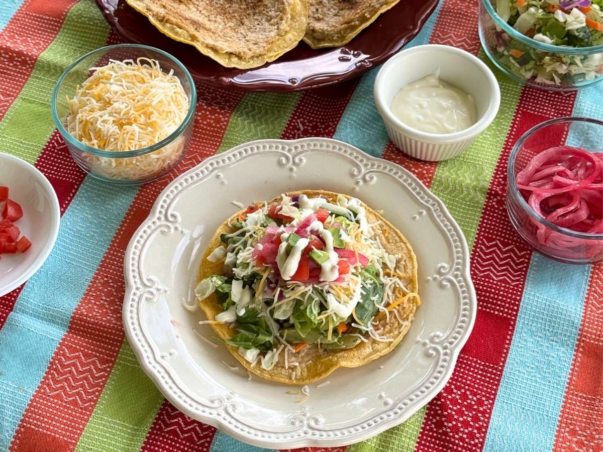 Crispy baked ground chicken taco topped with lettuce, tomatoes, avocado, shredded cheese, pickled red onions, and lime crema.