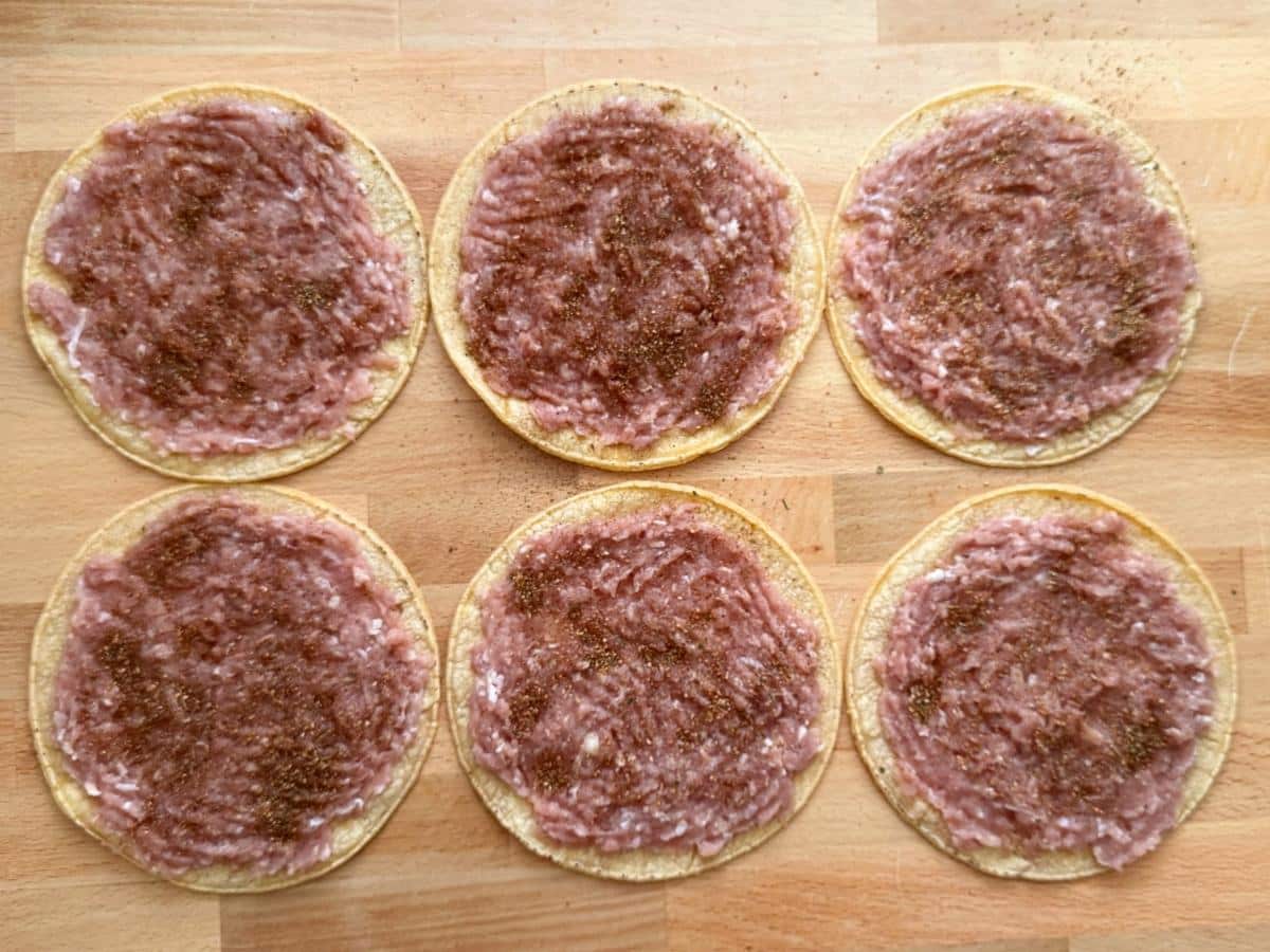 Ground chicken spread in a thin layer over corn tortillas and sprinkled with taco seasoning before baking.