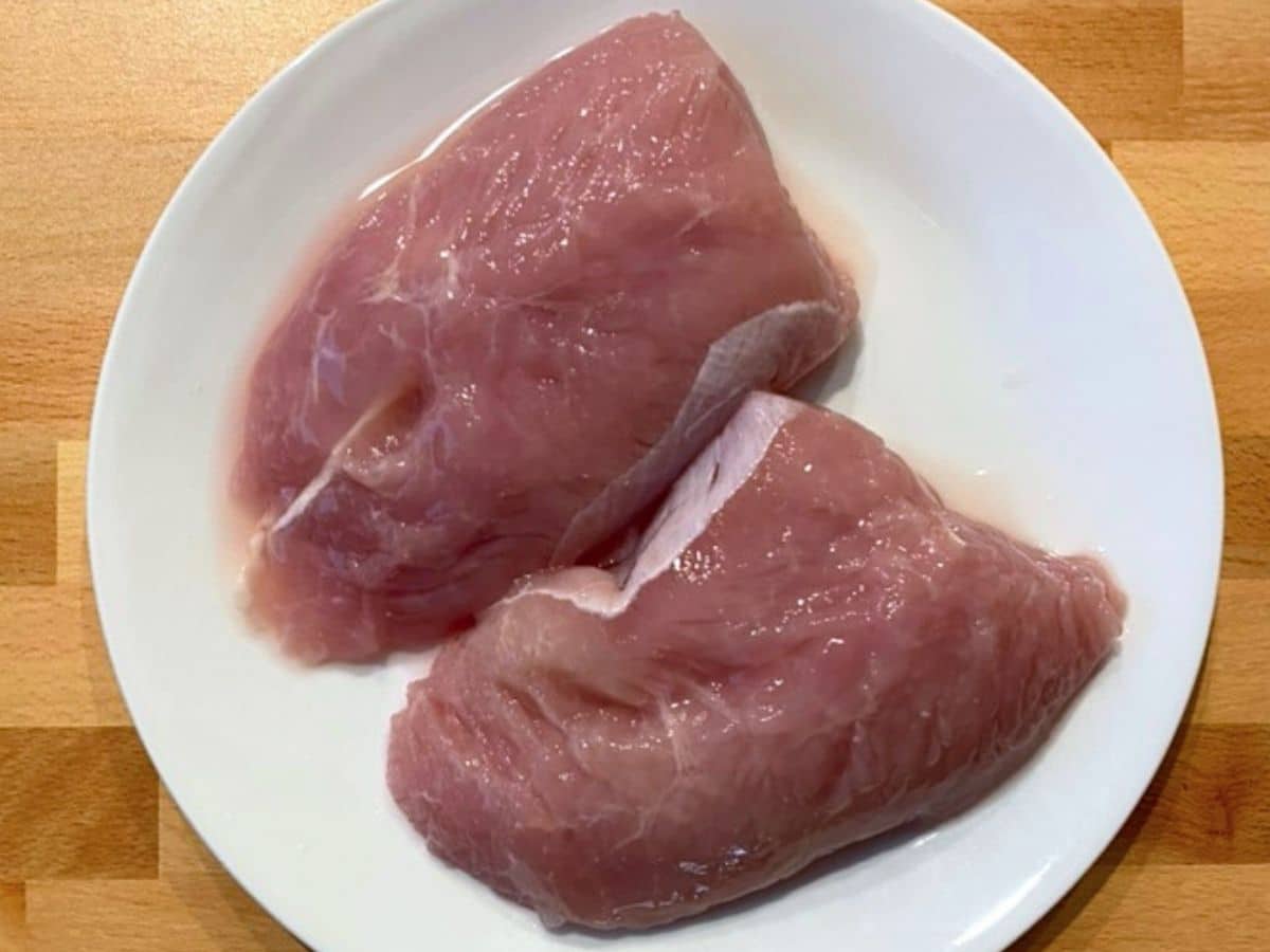 Two uncooked turkey tenderloins on a white plate.