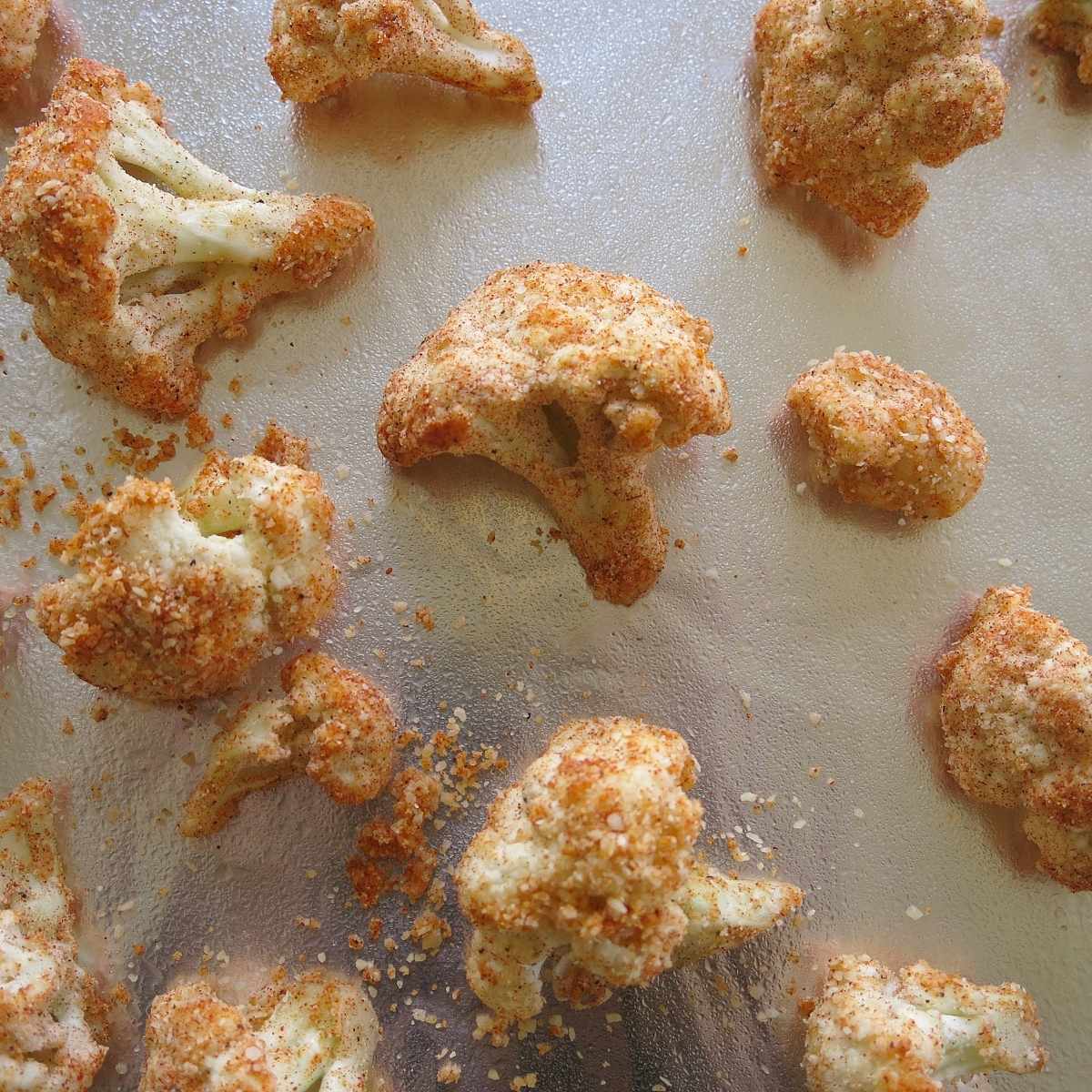 Parmesan-coated cauliflower florets arranged on a baking sheet before roasting.
