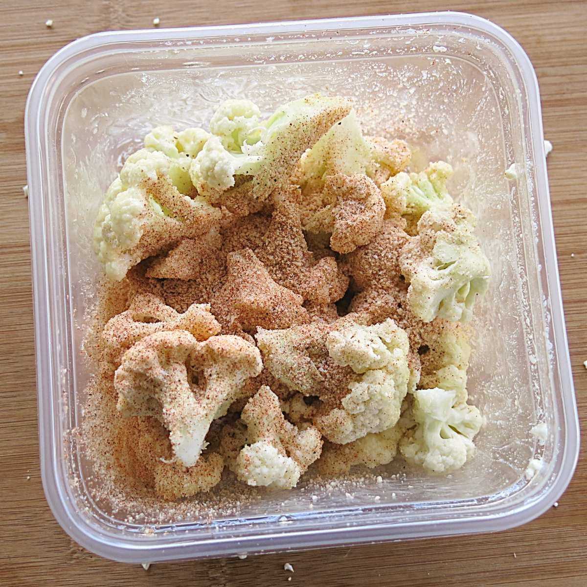 Cauliflower florets sprinkled with Parmesan, paprika, and black pepper before tossing.