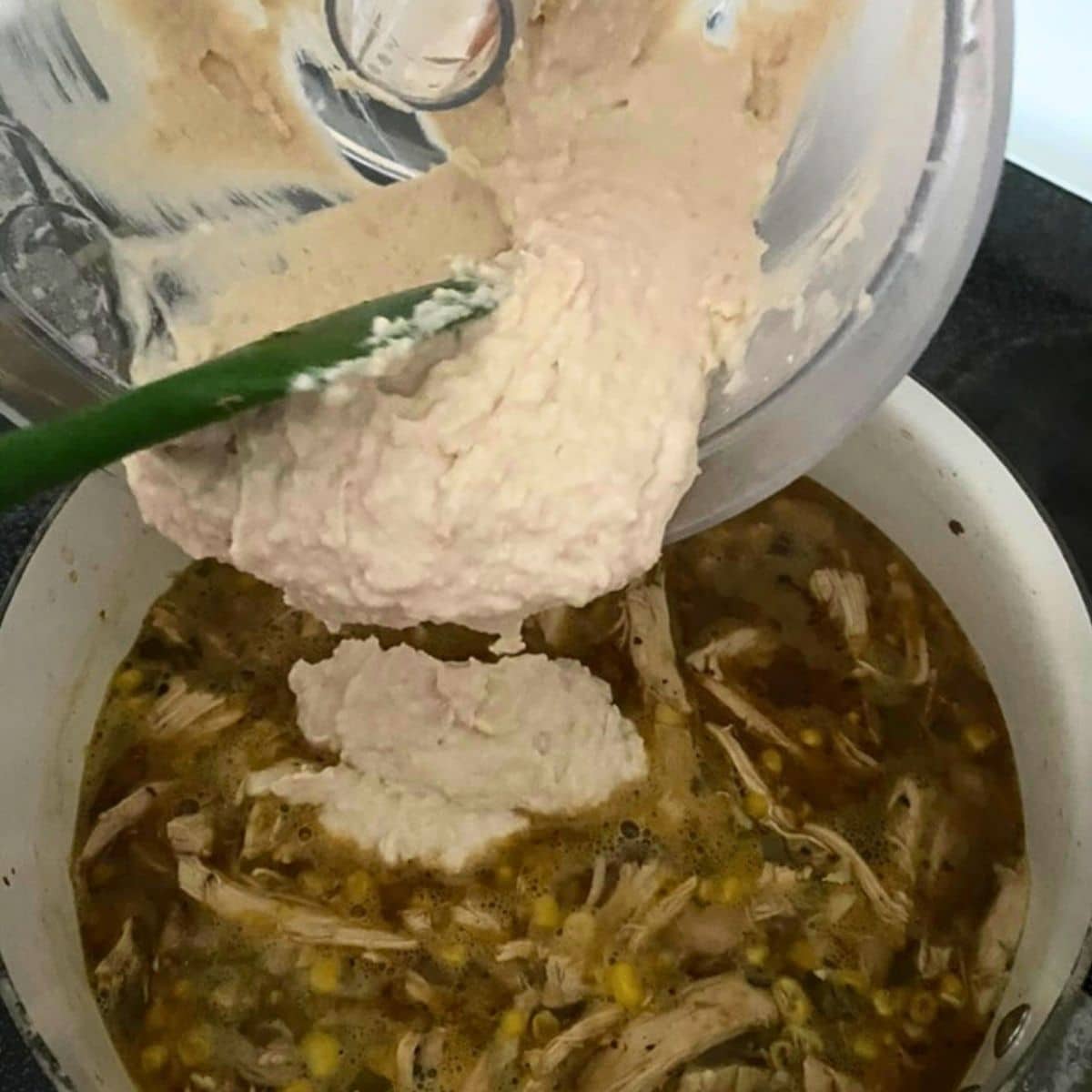 Blended white beans and cream cheese being added to white chicken chili for a thick, creamy broth.