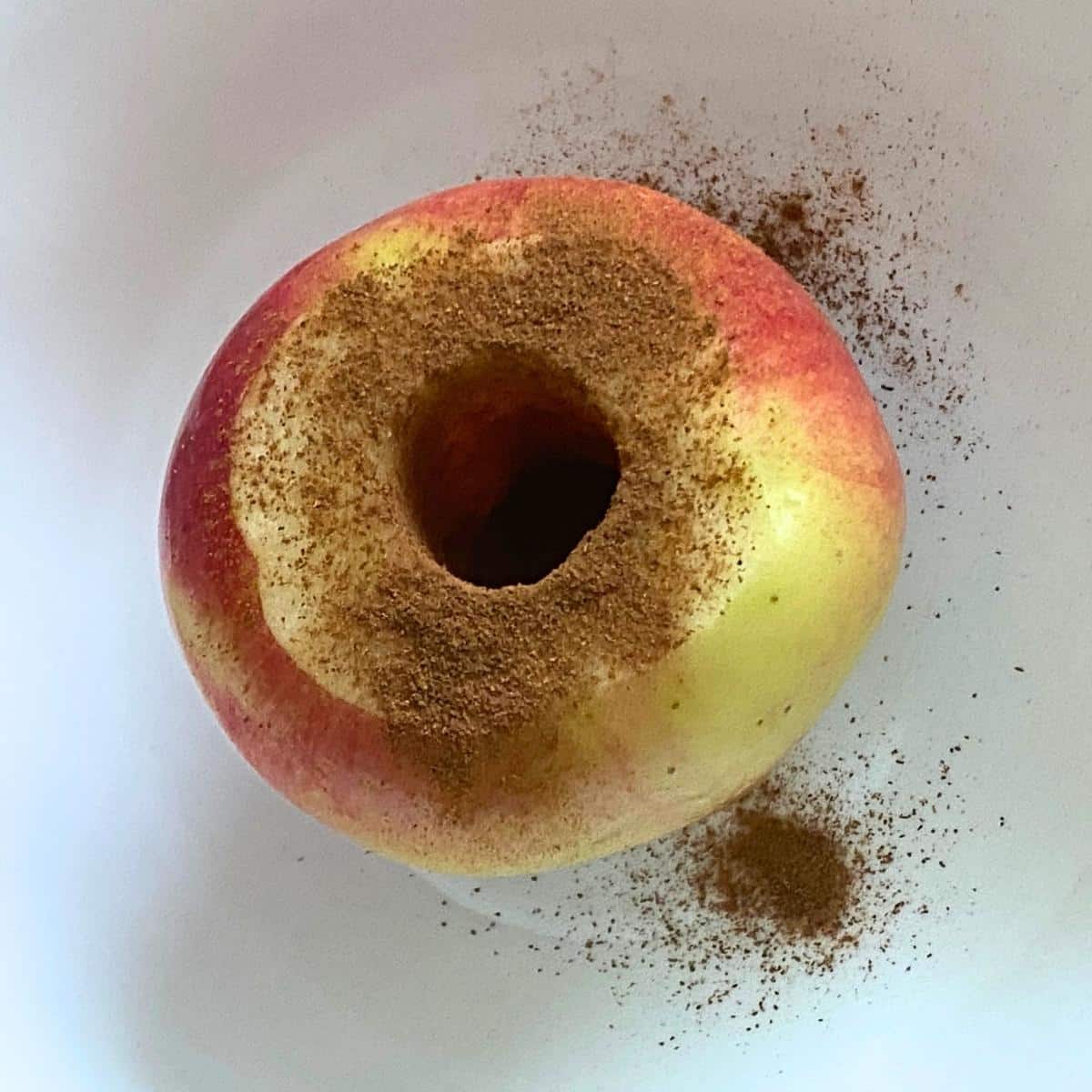Cored apple with part of the top peeled away and sprinkled with cinnamon.