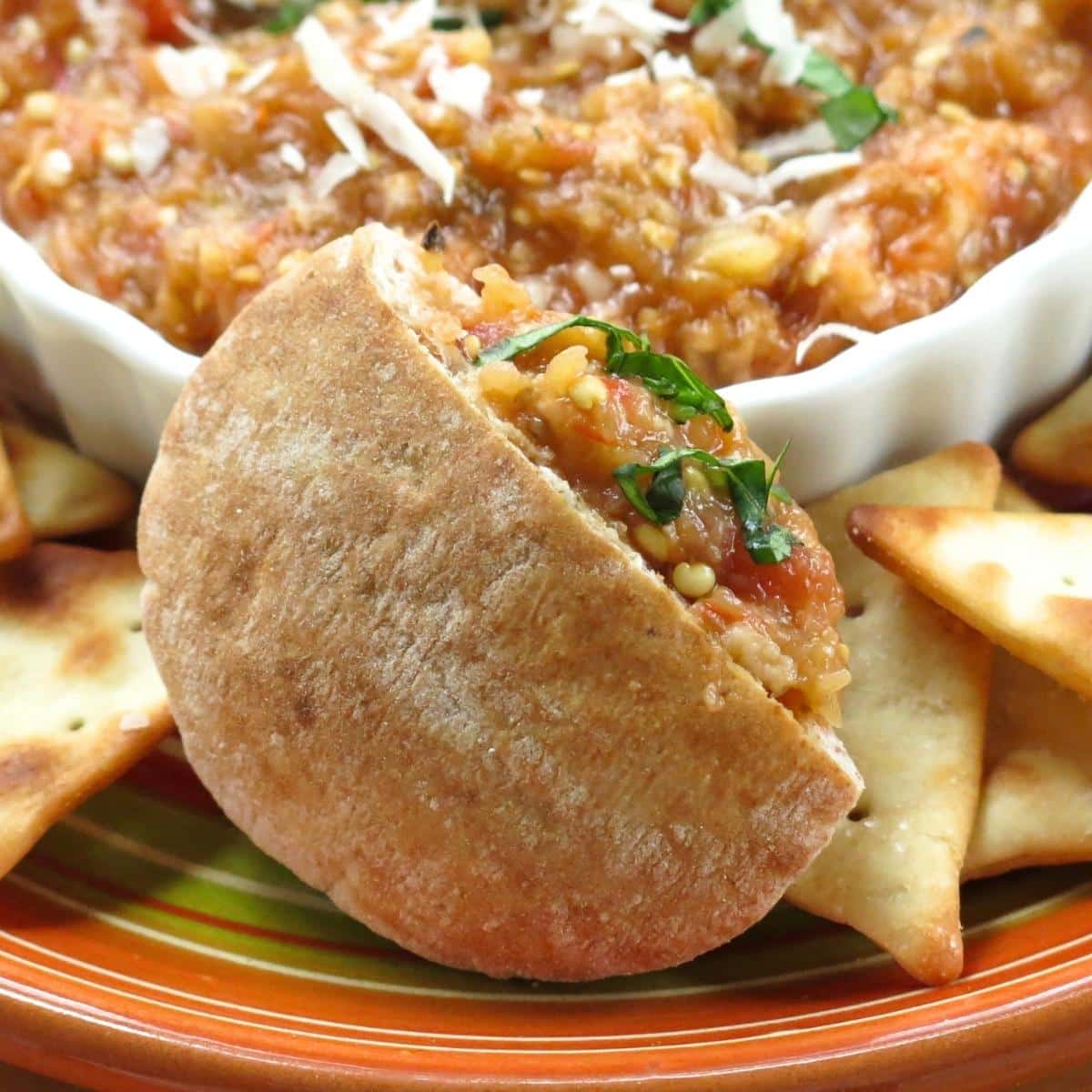 Eggplant Parmesan dip spooned into a mini pita pocket with pita chips and warm dip in the background.