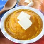 Mashed butternut squash in a bowl with 2 pats of butter on top.