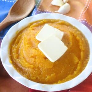 Mashed butternut squash in a bowl with 2 pats of butter on top.