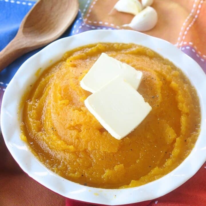 Mashed butternut squash in a bowl with 2 pats of butter on top.
