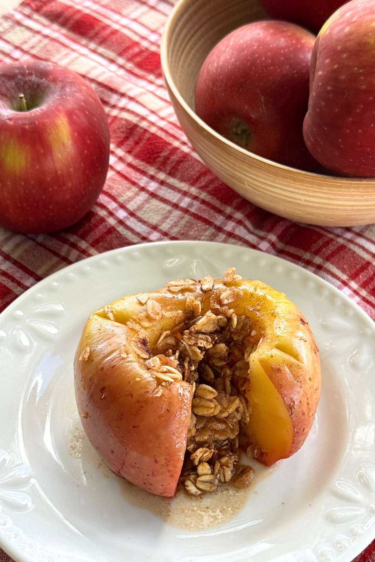 Microwave baked apple stuffed with cinnamon, oats and honey with a cut in front to expose filling and whole apples in the background.