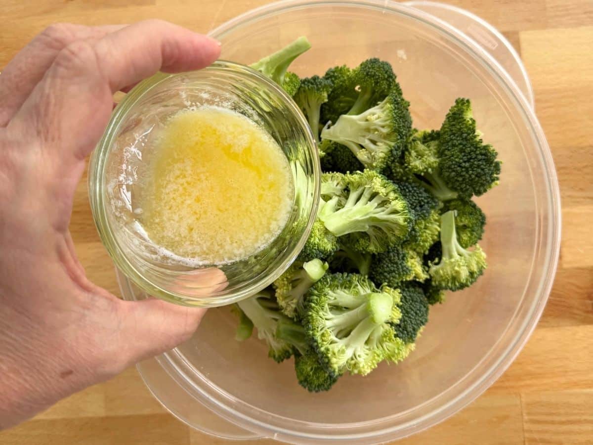 Melted butter being added to fresh broccoli florets for crispy Parmesan broccoli bites.