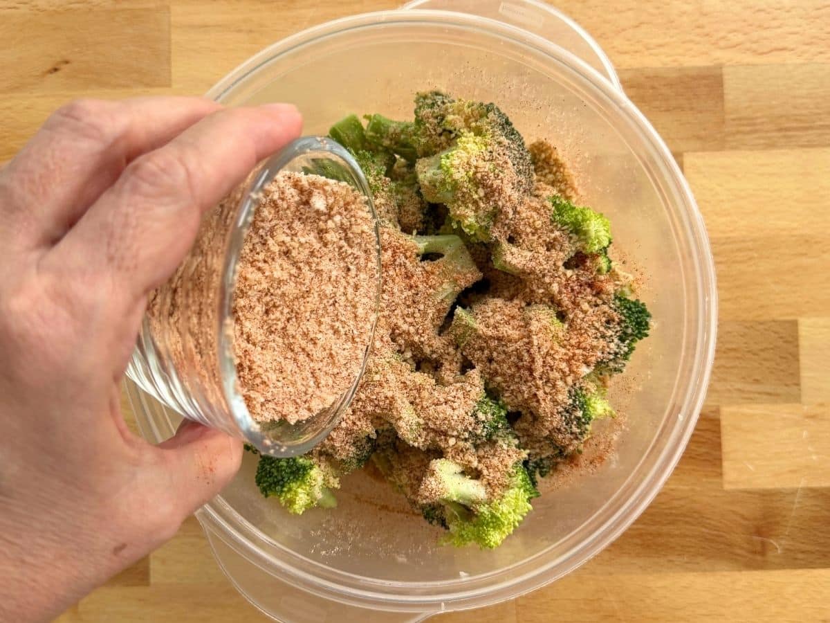 Parmesan cheese and seasoning mixture being added to butter-coated broccoli florets.