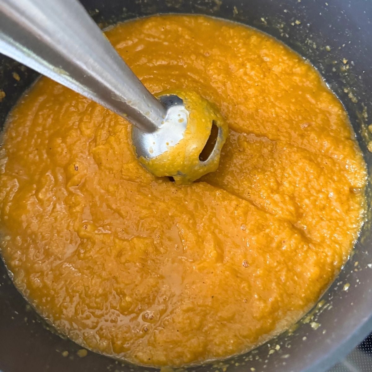An immersion blender pureeing the soup until smooth and creamy.