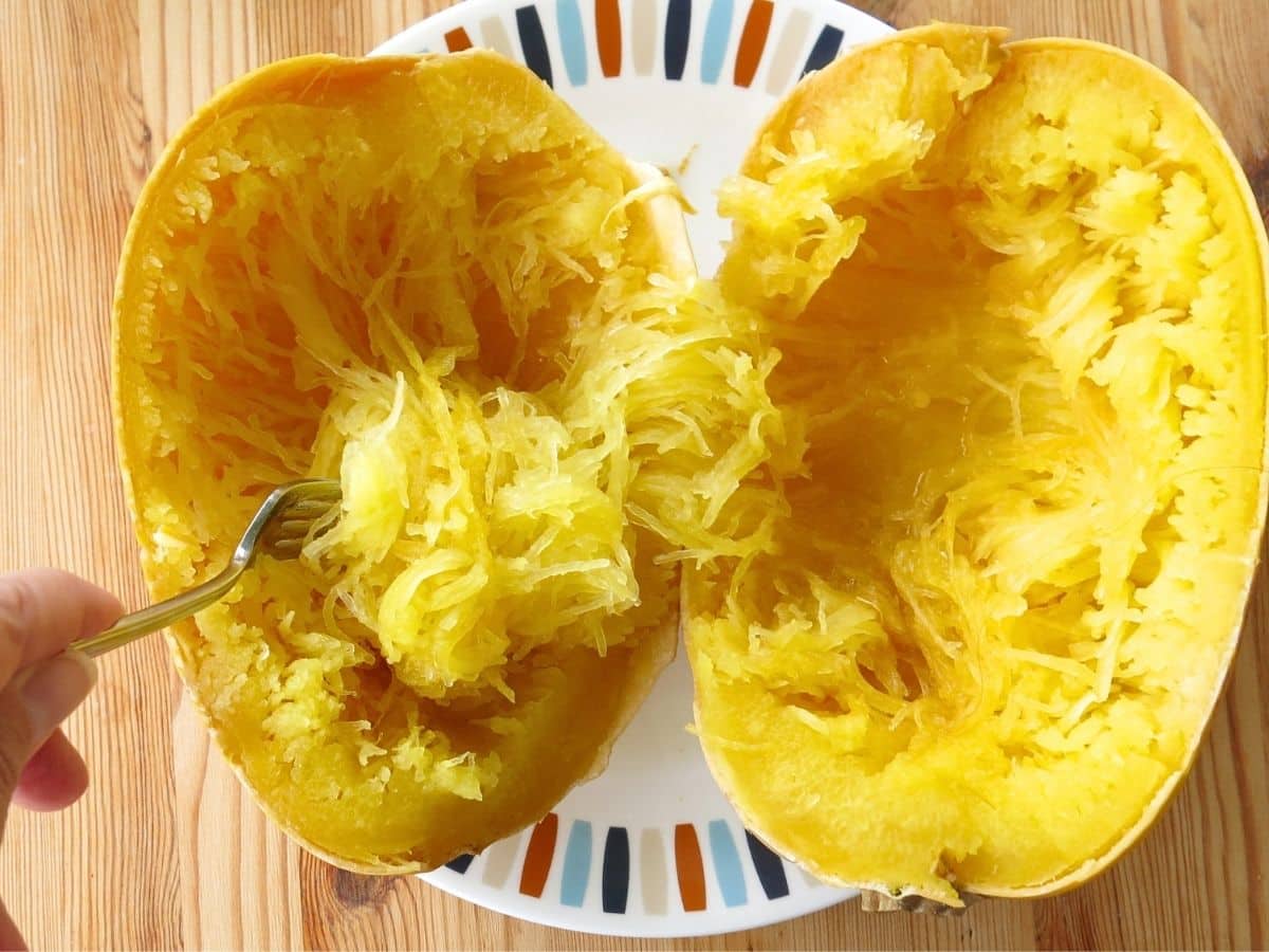 Fork removing strands from a spaghetti squash cut lengthwise.