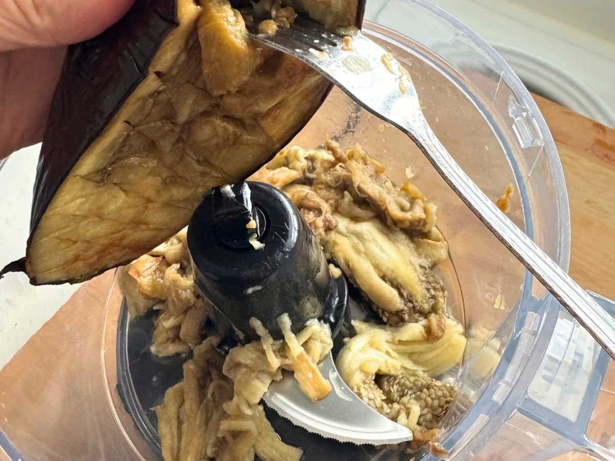 Roasted eggplant flesh being scraped from the skin into a food processor.