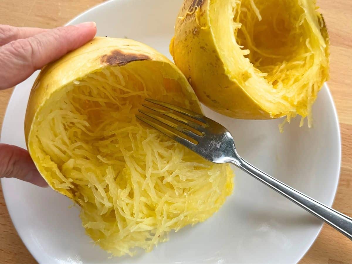 Fork removing strands from a spaghetti squash cut crosswise.