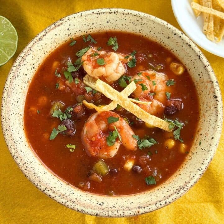 Shrimp tortilla soup with black beans, corn, cilantro, and crispy tortilla strips in a tomato broth.