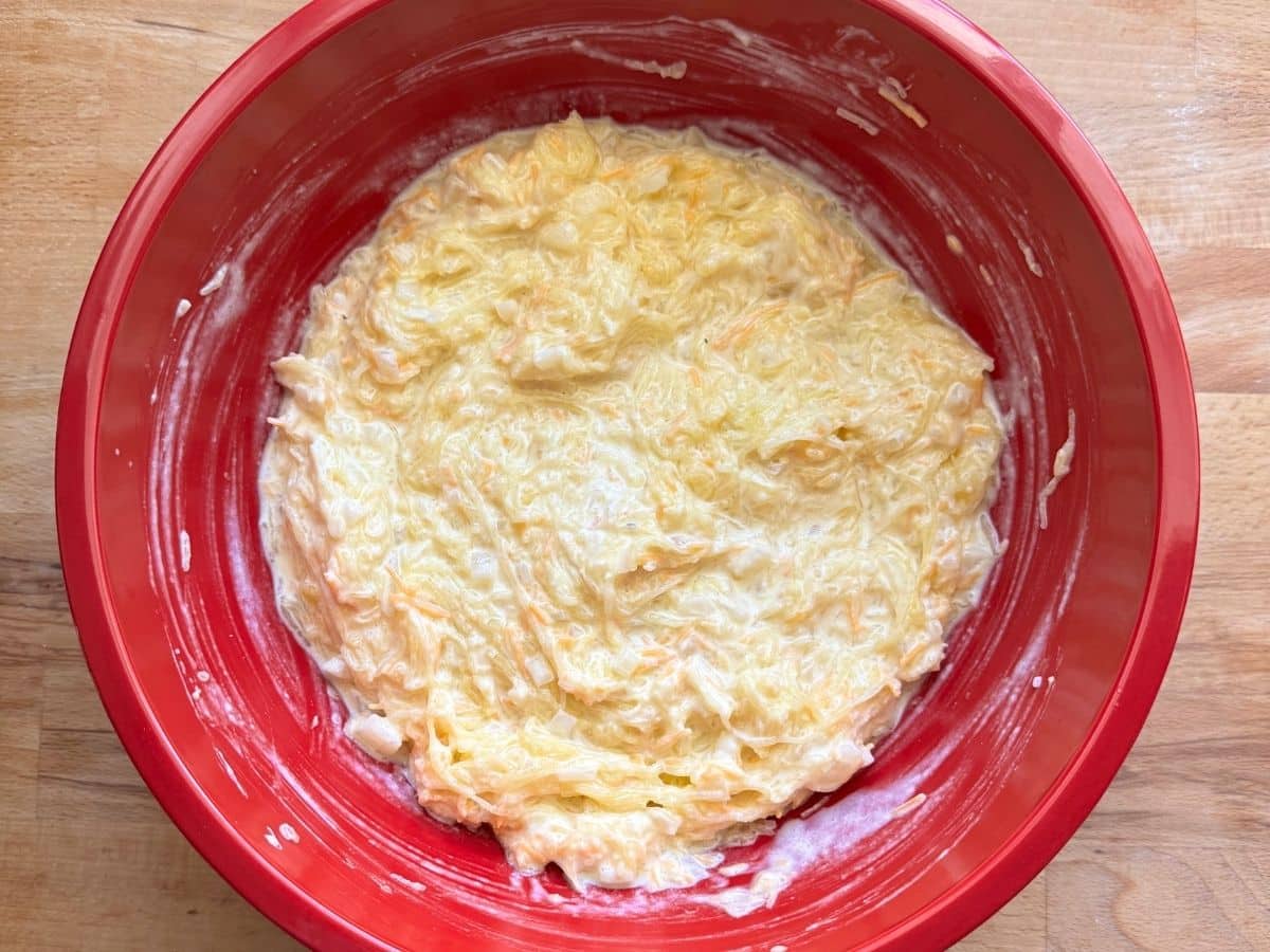Spaghetti squash, sour cream, eggs, cheddar cheese, and sautéed onions mixed in a bowl.