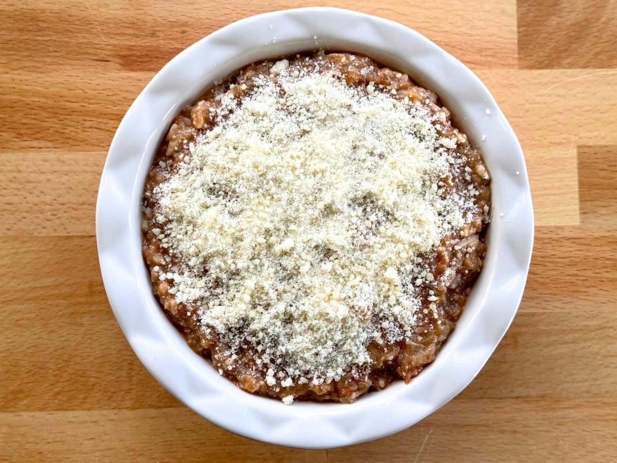 Eggplant Parmesan dip in a baking dish topped with grated Parmesan before baking.